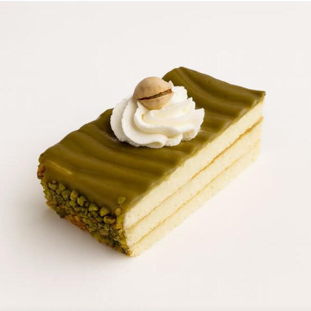 Pistachio Cake Slice $7.49 Layered pistachio cake slice coated in green pistachio glaze, edged with crushed pistachios and topped with a whipped cream swirl.