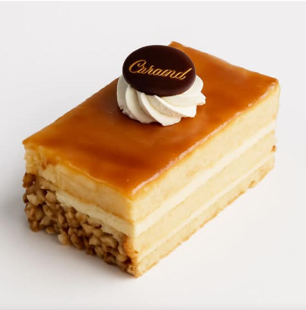 Caramel Cake Slice $7.49 Layered sponge and cream with a caramel glaze, finished with chopped nuts on the side, a cream swirl, and a chocolate disc.